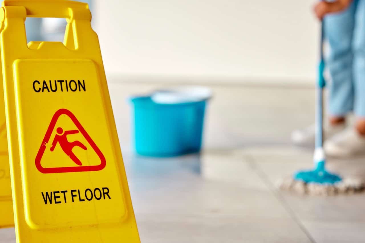 wet floor sign while person mops floor to prevent slip and falls