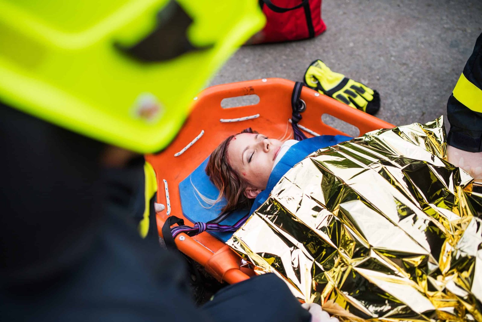 A young injured woman in a plastic stretcher after a catastrophic car accident, covered by thermal blanket. 
